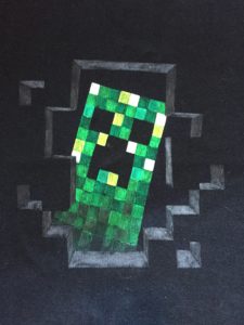 Motiv eines Computerspiels, Creeper mit verschiedenen Grüntönen an Stoffmalfarbe auf einen Pullover aufgemalt